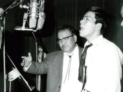 古賀政男（左、65歳ごろ）と大川栄策（右、20歳）。レコーディング中に歌唱指導する様子